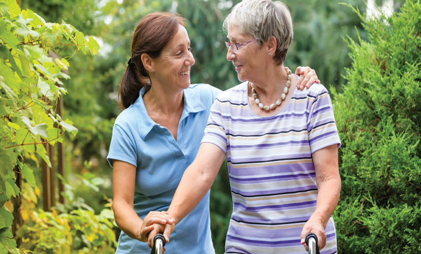 Woman puts arm around elderly woman's shoulder during a walk outside.